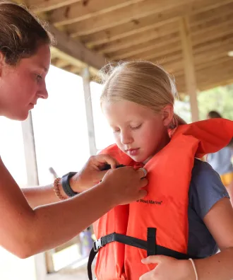 Counselor helping camper with her life jacket