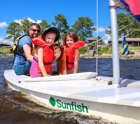 Dad and two girls enjoying time together on a sailboat at family camp