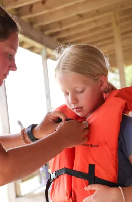 Counselor helping camper with her life jacket