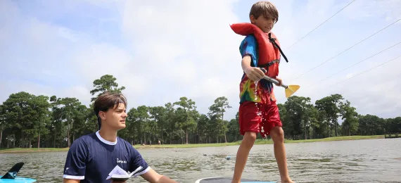 Counselor teaching a boy to paddle board