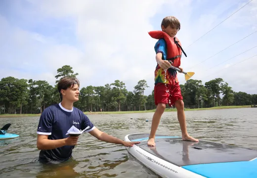 Counselor teaching a boy to paddle board
